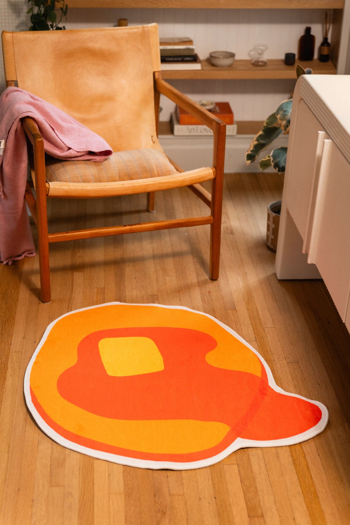 3' × 3' pancake-shaped rug with orange syrup, yellow butter, and white outline beside a wooden chair and white cabinet.