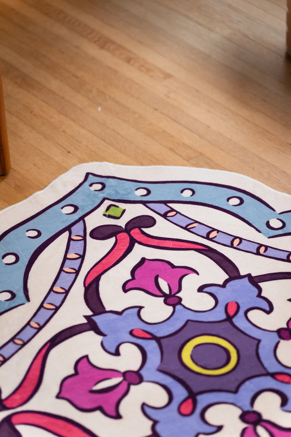 Scalloped edge rug on wood floor with a dusty blue dotted border, cream panels, and magenta floral details.