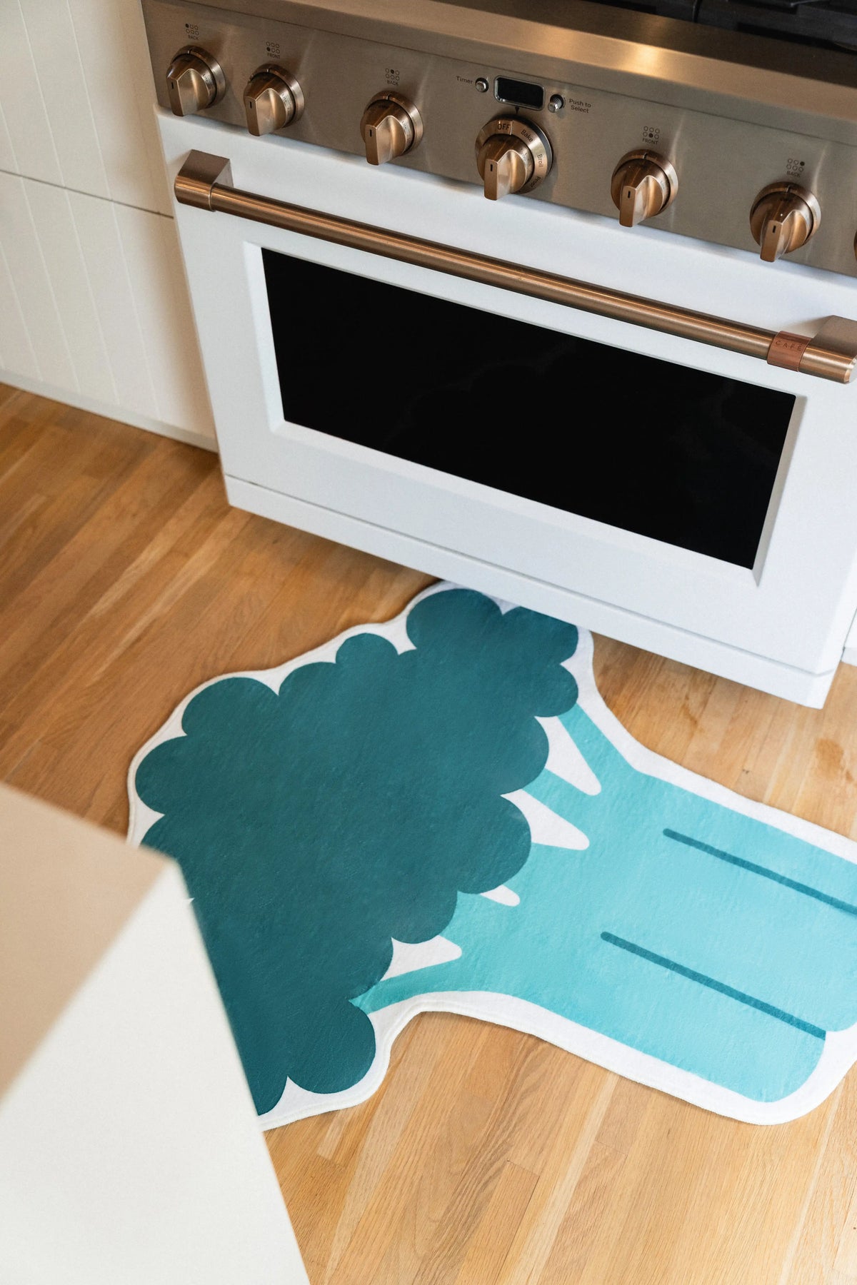 3' × 3.5' Green Irregular Broccoli Shaped Rug by Becca Franks with dark green florets, a teal stem, and white border in front of a white oven.