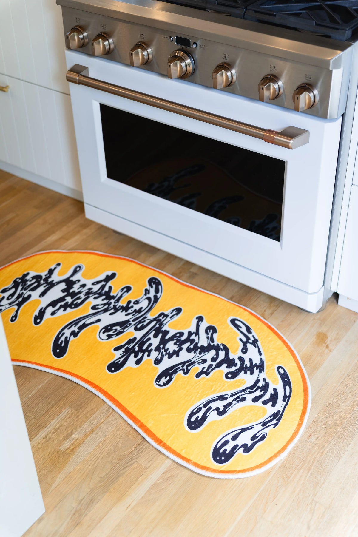 From above, dense black strokes break apart into white channels across the rug’s yellow surface.