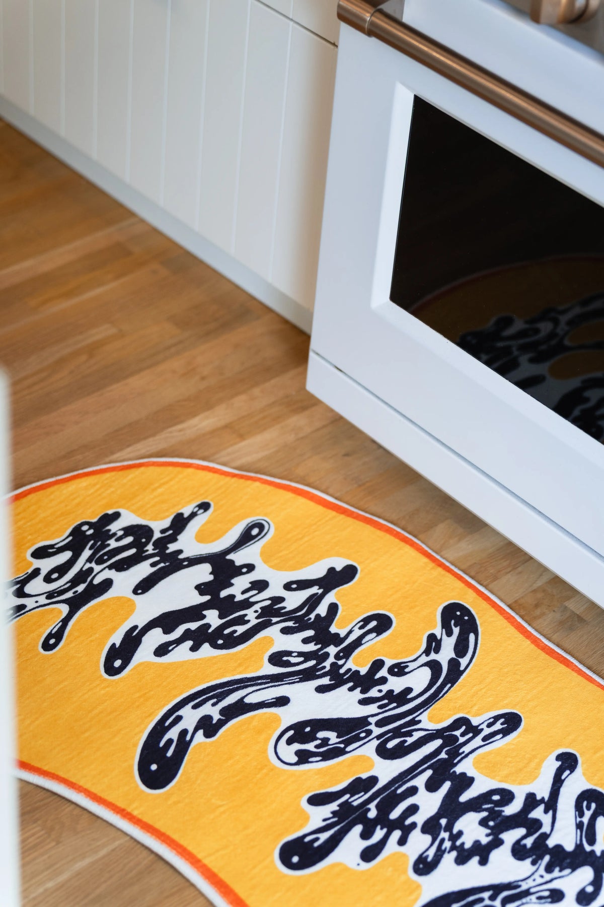A cropped view by the oven follows the black curls as they spread toward the orange-bound edge.