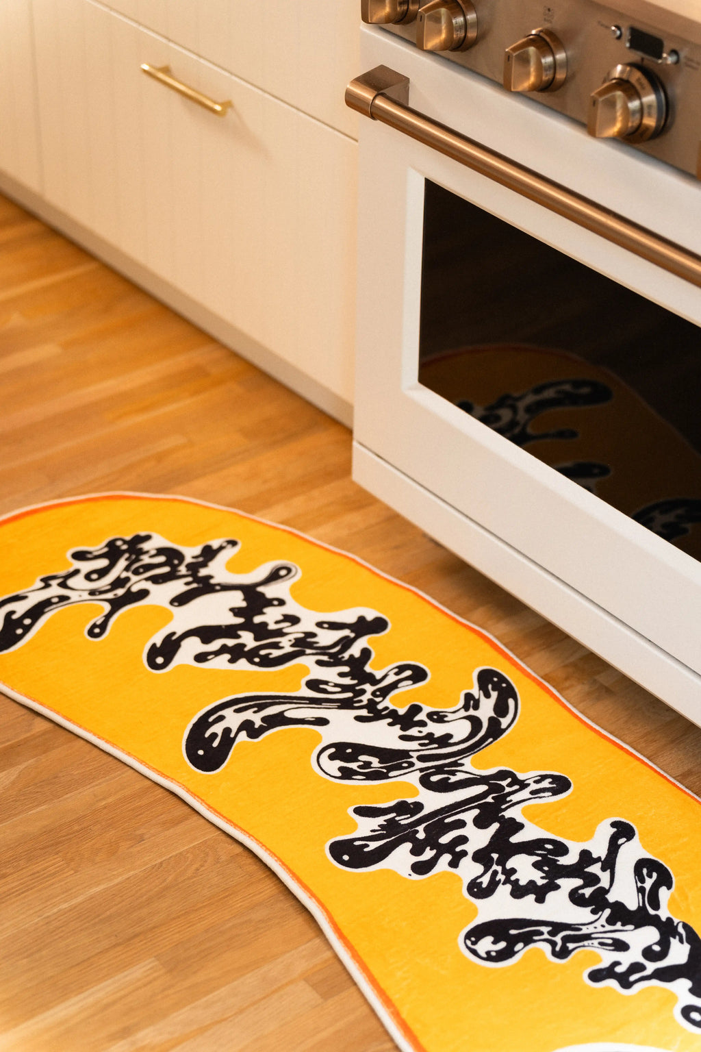 The golden runner turns slightly along white cabinets, carrying its ink-like motif past the oven door.