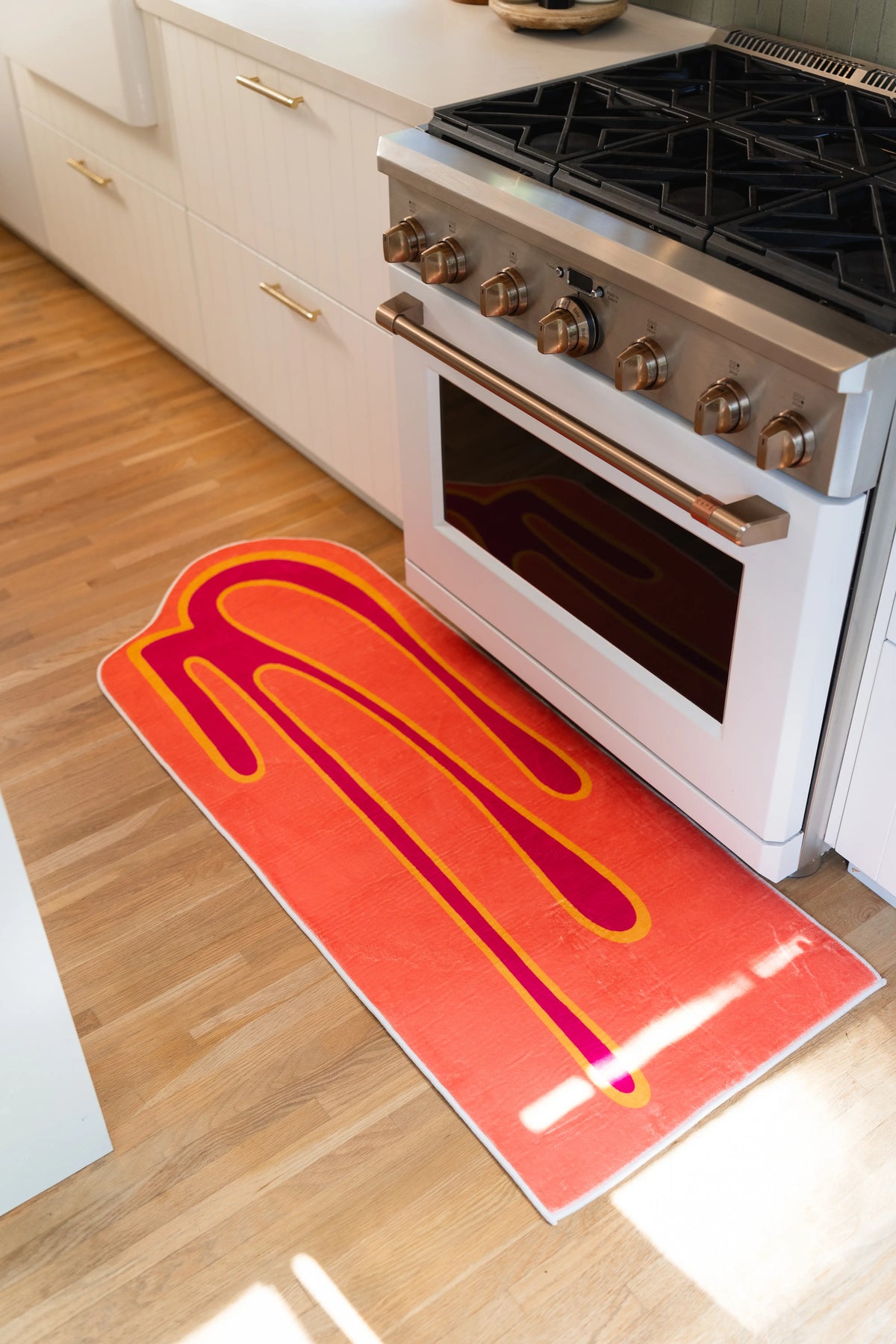 Angled view of an orange runner rug with a magenta melting stripe beside a white oven.