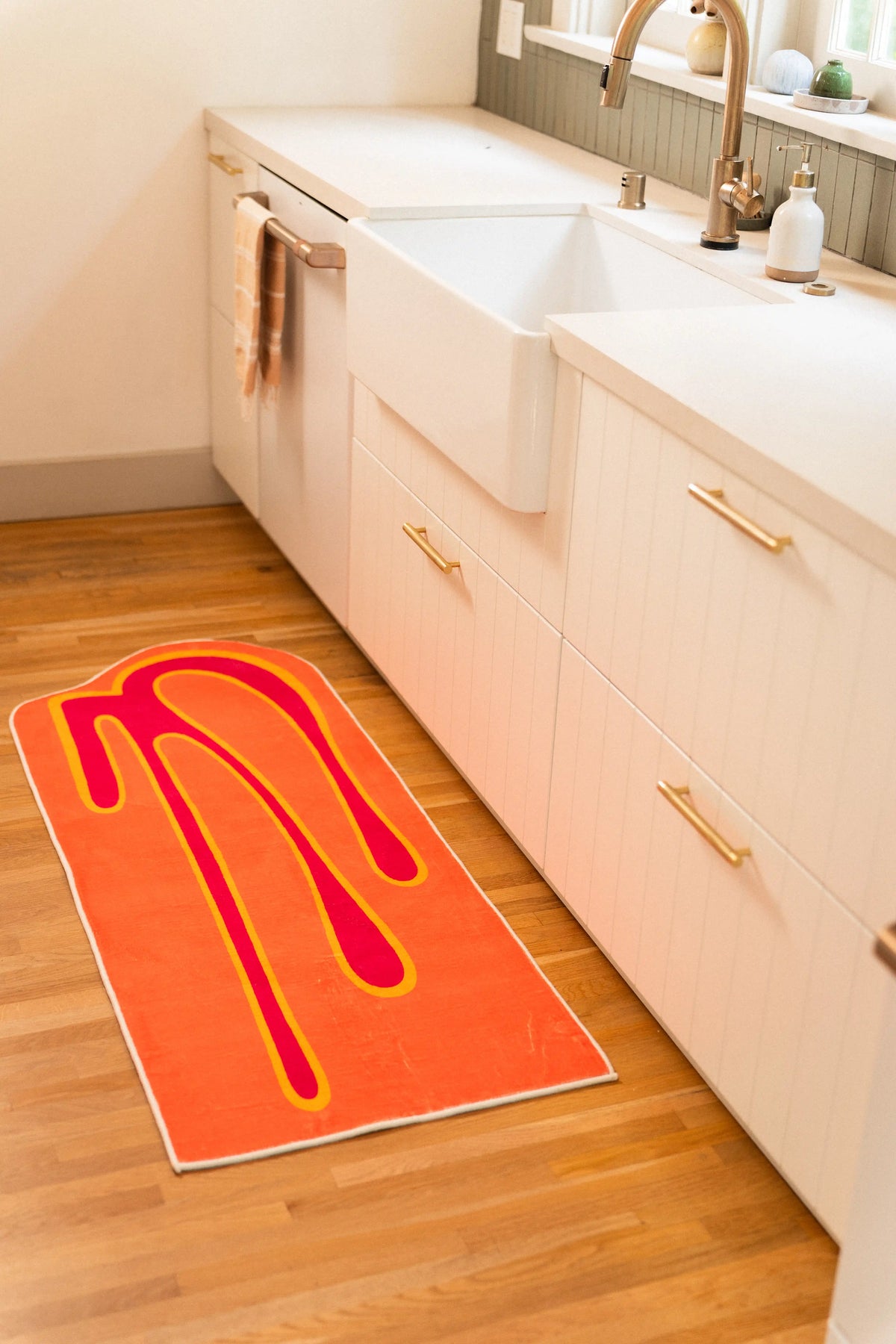 Orange abstract runner beside white kitchen cabinets and a farmhouse sink on wood flooring.