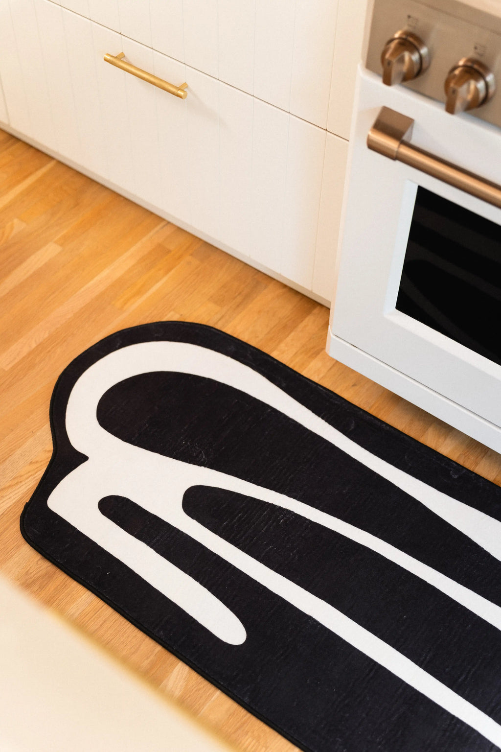 Rounded end of a black and white abstract runner beside a white oven on light wood flooring.