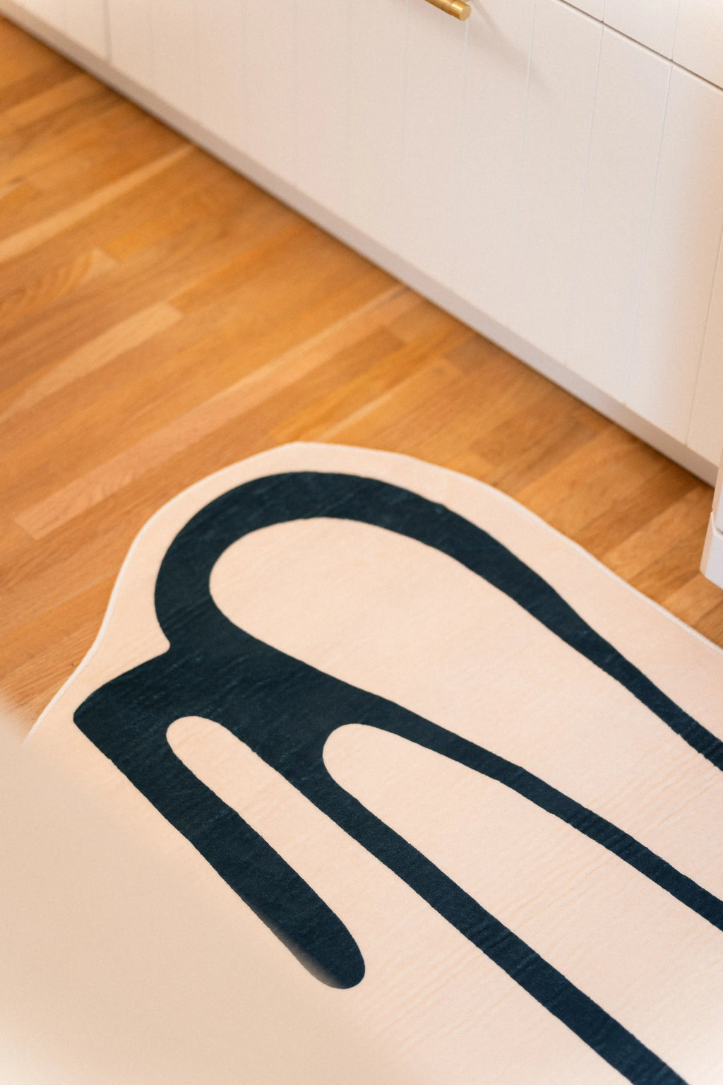 Close-up of the rounded green drip pattern at the end of a beige kitchen runner beside white cabinetry.