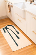 Beige abstract runner placed along white cabinets and a farmhouse sink on light wood flooring.