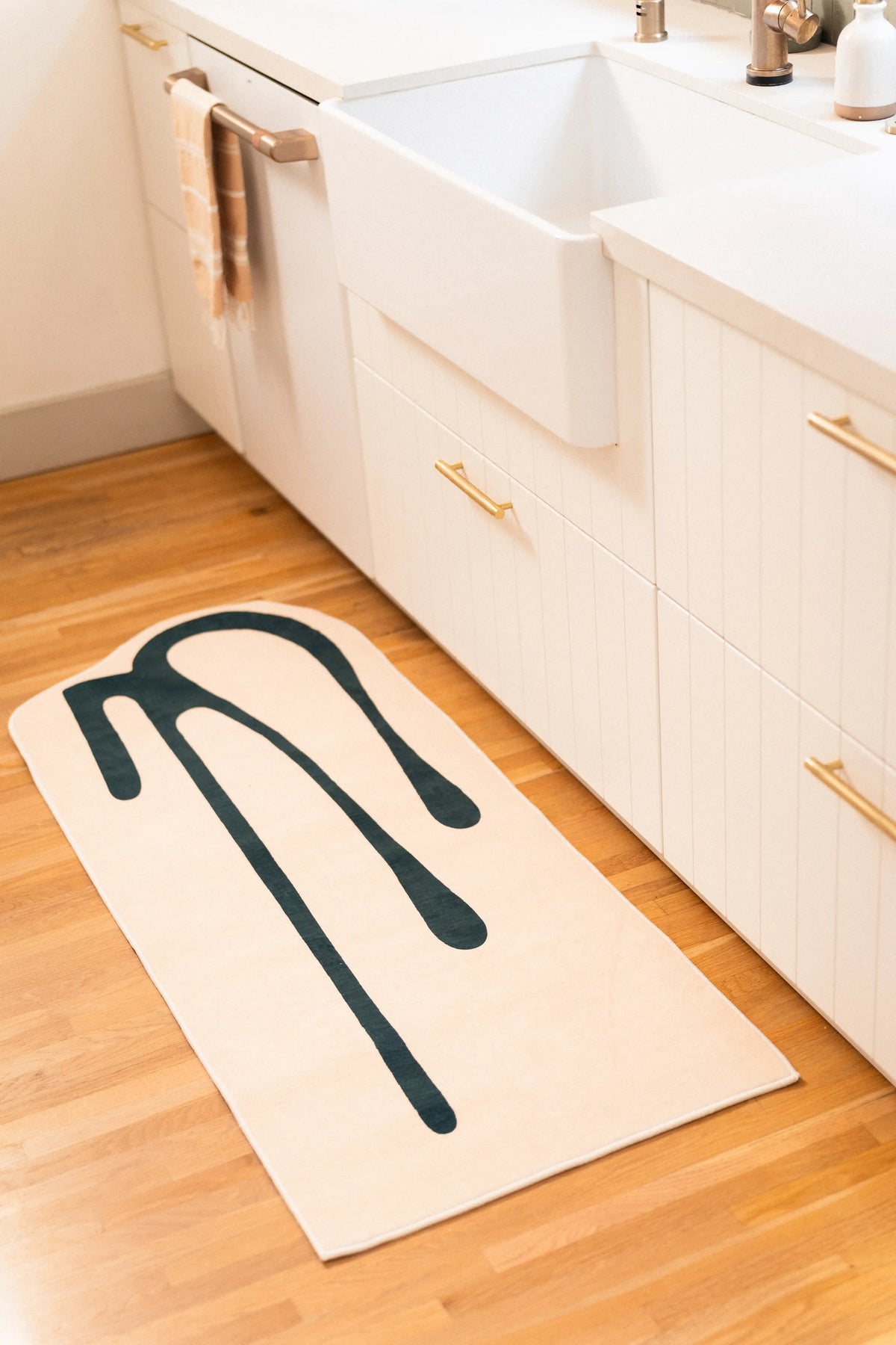 Beige abstract runner placed along white cabinets and a farmhouse sink on light wood flooring.
