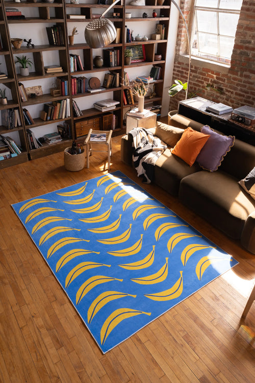 Blue banana runner rug laid out in sunny living room near sofa and bookshelves, on wood floor