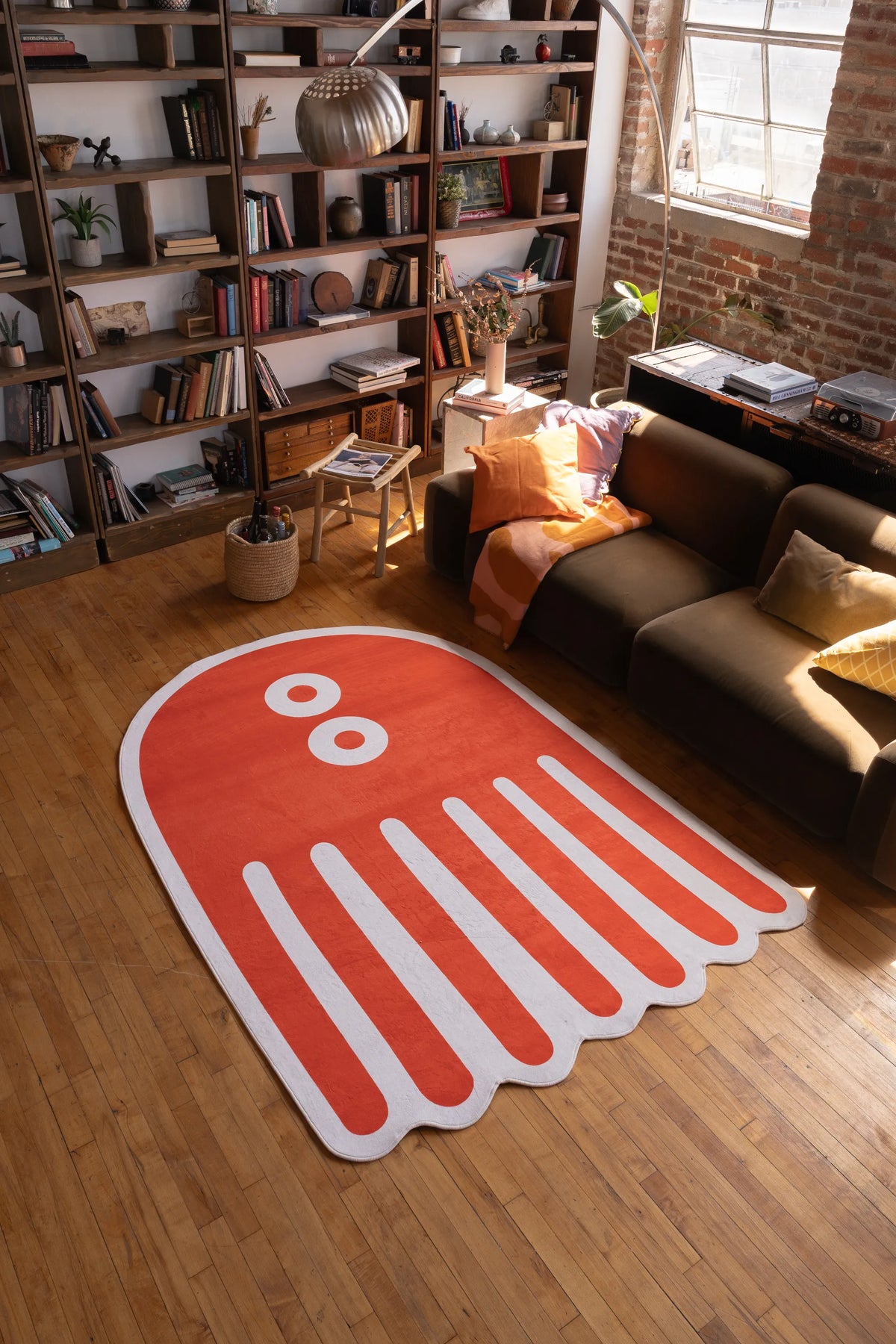Large orange abstract octopus rug in 5x7 size on wooden floor in cozy living room with bookshelf and warm lighting