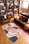 Abstract mosaic rug in pink, navy, and mustard tones styled in a cozy living room with wood floors and built-in bookshelves