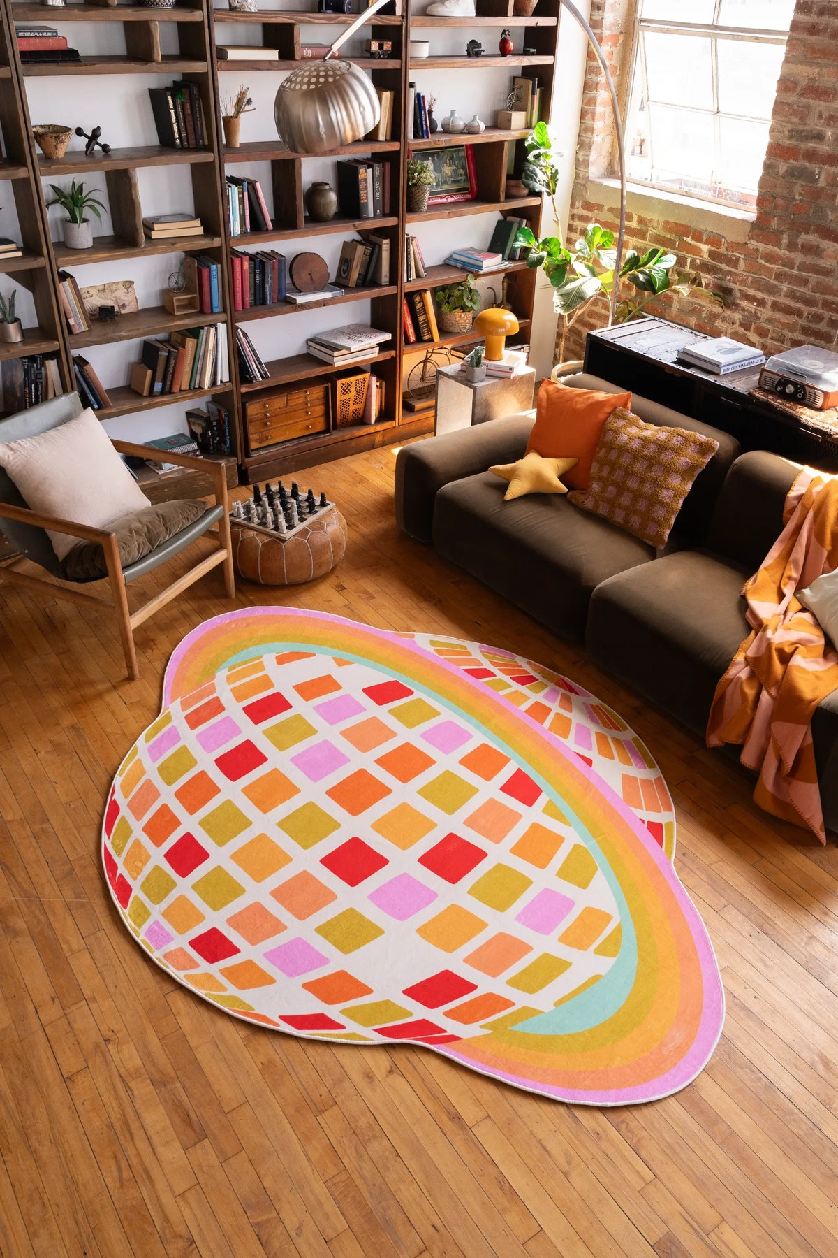 Orange Disco Planet Checkered Rug by Darra Sargnt laid out on warm wood flooring beside a sofa with layered textiles