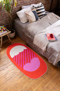 Red Mouth Pop Art Rug by Becca Franks beside bed in bold, cozy bedroom with wood floor