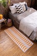 Banana runner rug aligned neatly beside a bed, accenting warm-toned wood floor in a soft-lit setting