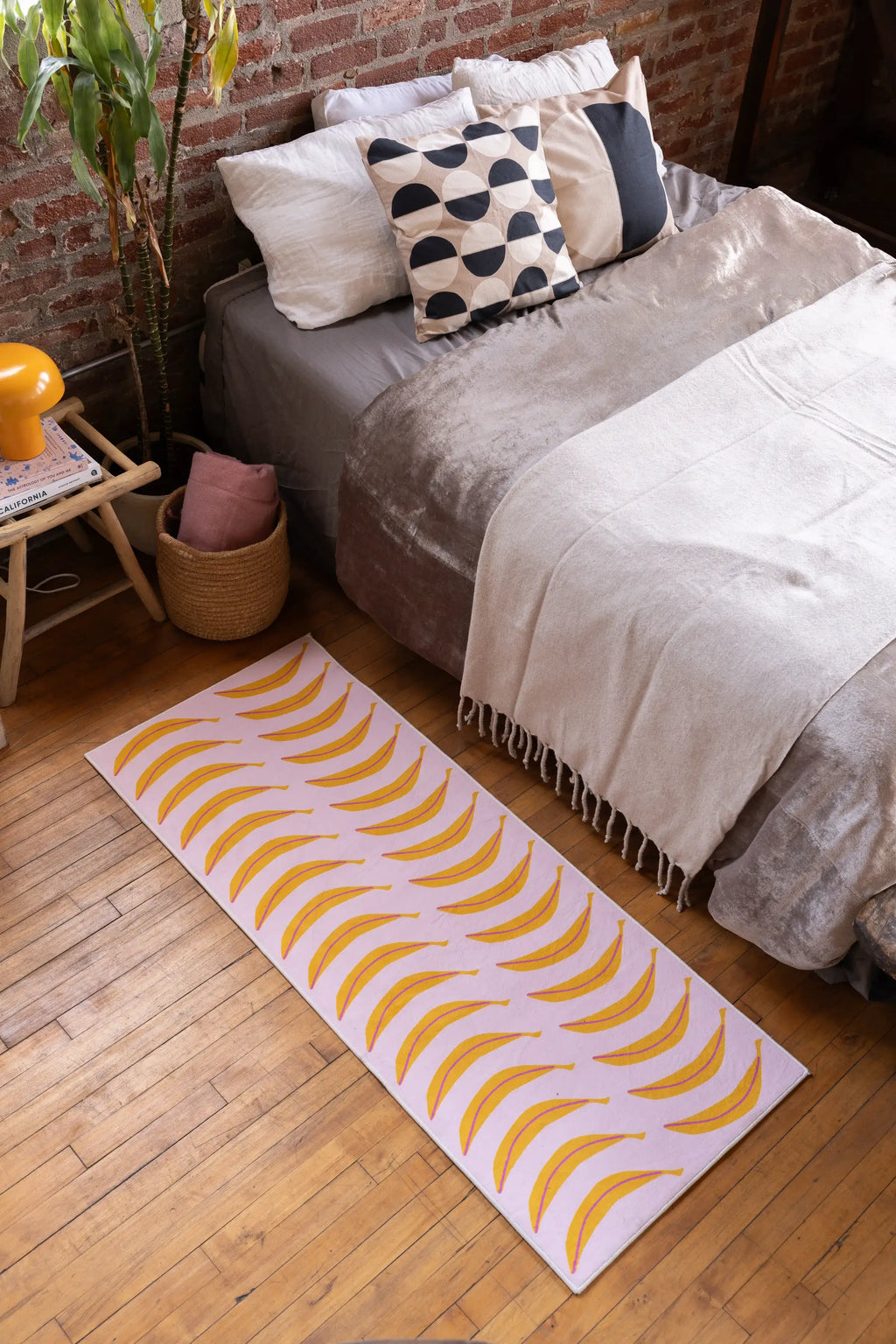 A Pink Banana Parade Funky Runner by Becca Franks stretches along the bed on warm wood flooring against a brick wall backdrop