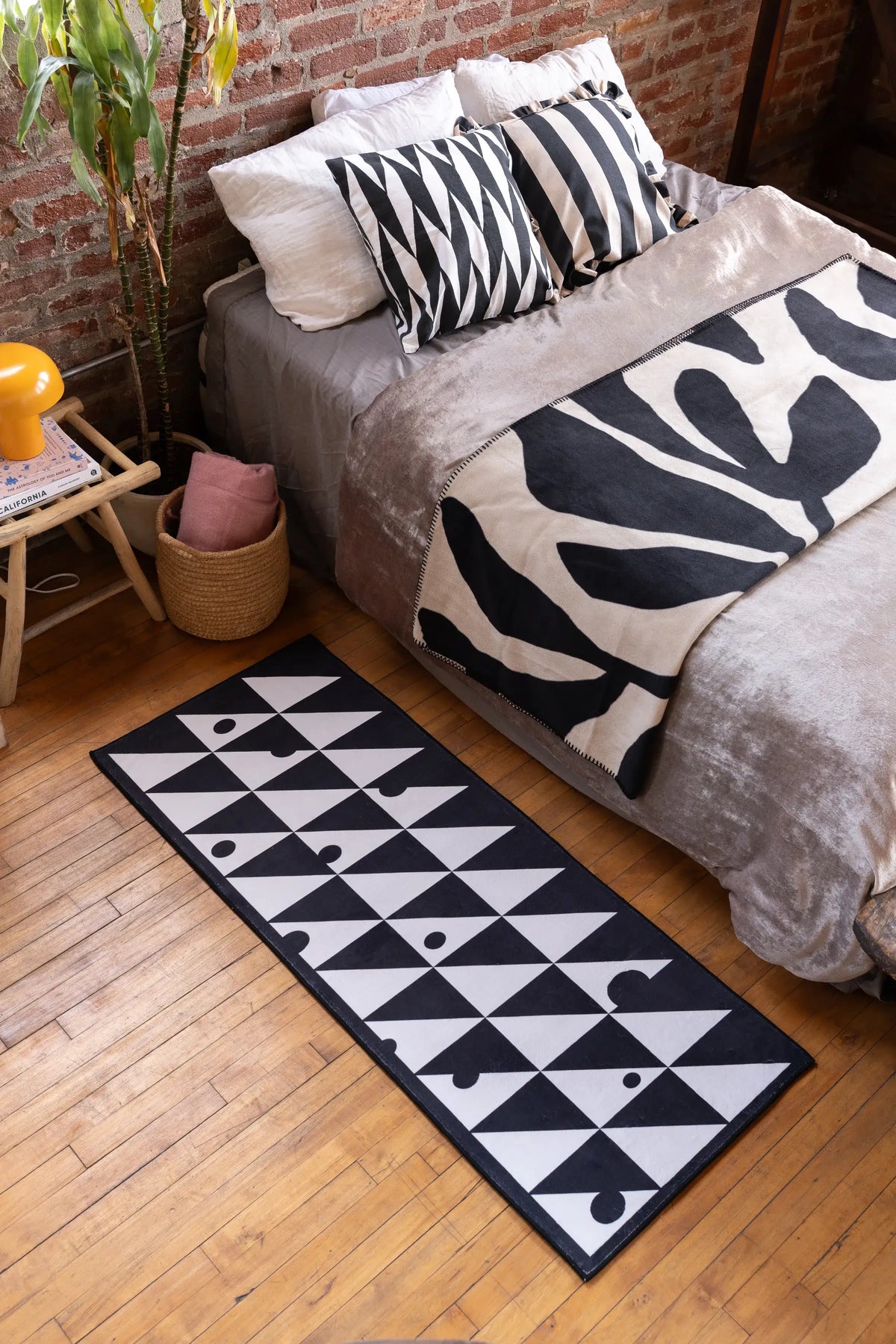 Black & White Triangle Dance Rug by Becca Franks placed beside a cozy bed with matching monochrome decor and soft lighting