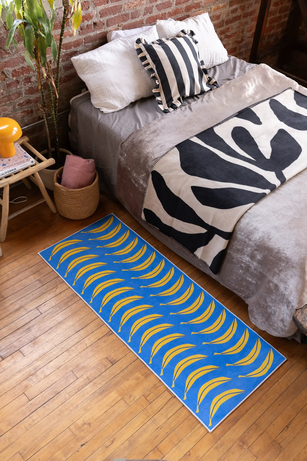 Blue Banana Parade Funky Runner by Becca Franks styled beside bed with zebra blanket, on wood floor