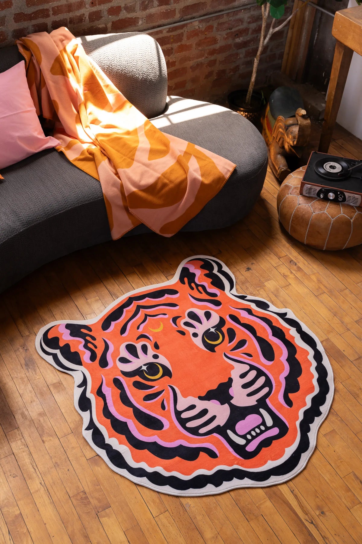 Funky tiger rug in bold orange and pink, laid out in a cozy nook with wood floor and exposed brick wall.
