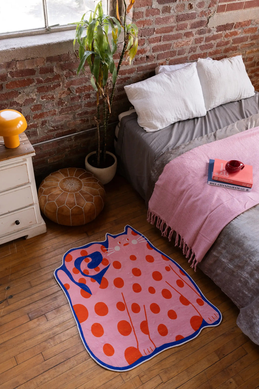 Navy blue Polka dots Funky Cat Rug by Becca Franks beside a low bed in a brick-walled bedroom with wood floor