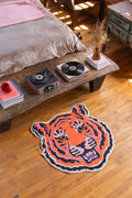 Funky tiger rug by a rustic low table and bed, on warm-toned wood floor in a sunlit loft-style bedroom.