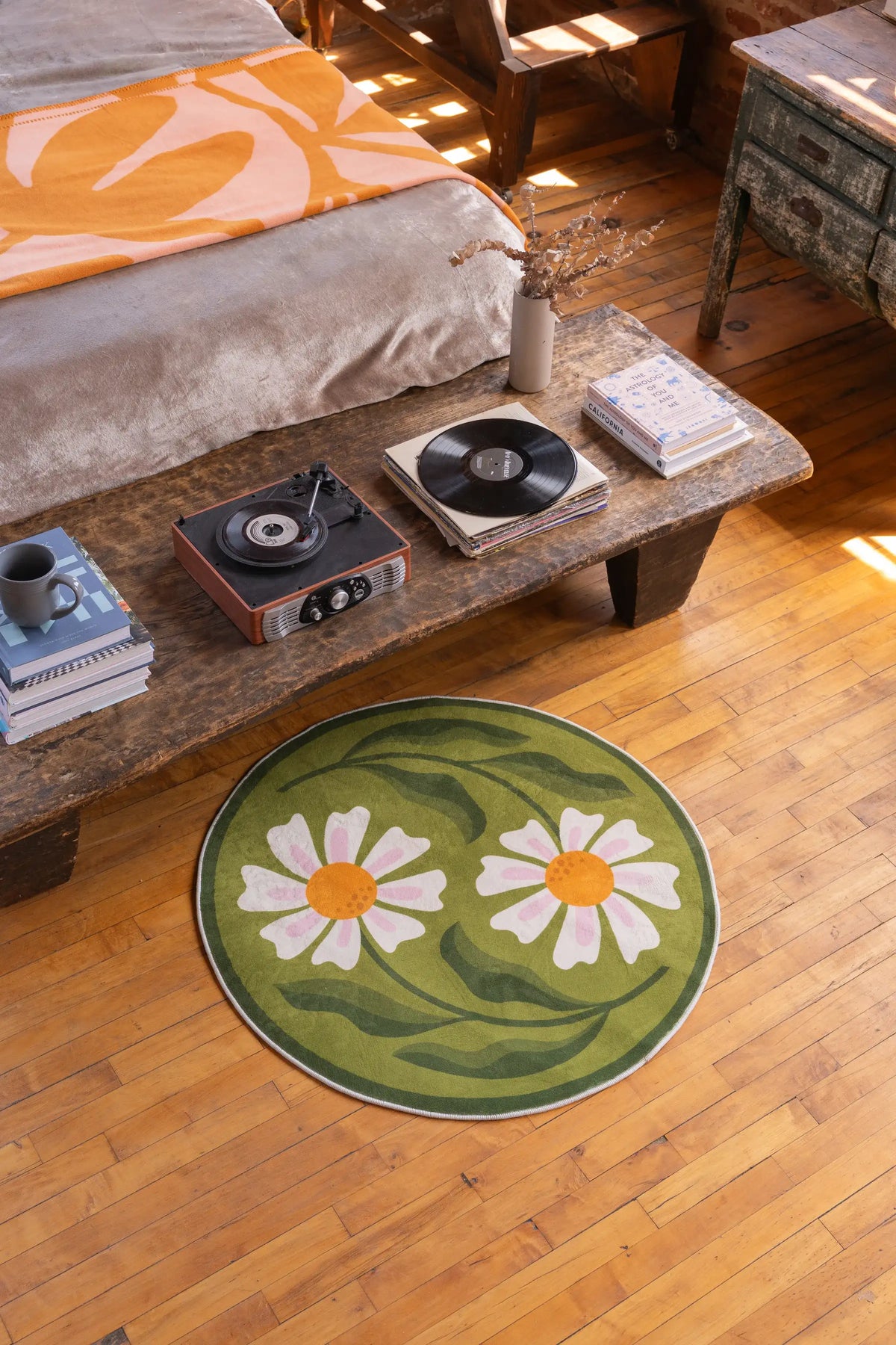 Green daisy rug adds a soft botanical charm to the bedroom with wooden floors and a rustic coffee table.