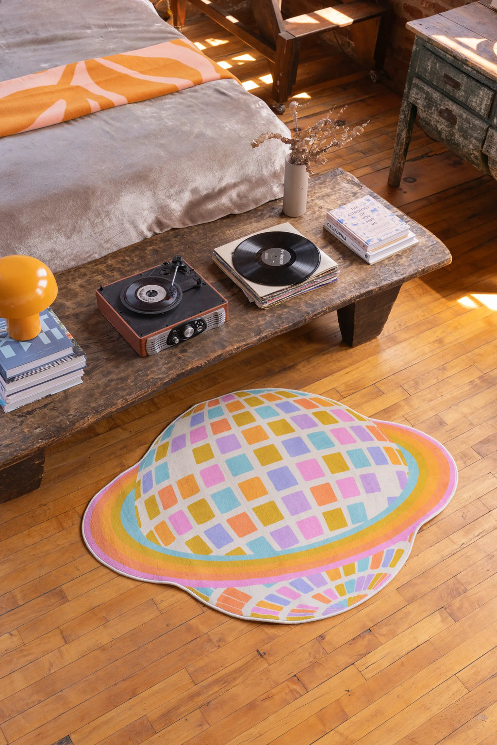 Colorful Disco Planet Checkered Rug by Darra Sargnt placed near a low wood table, nestled beside a cushioned seat on warm-toned wood floor