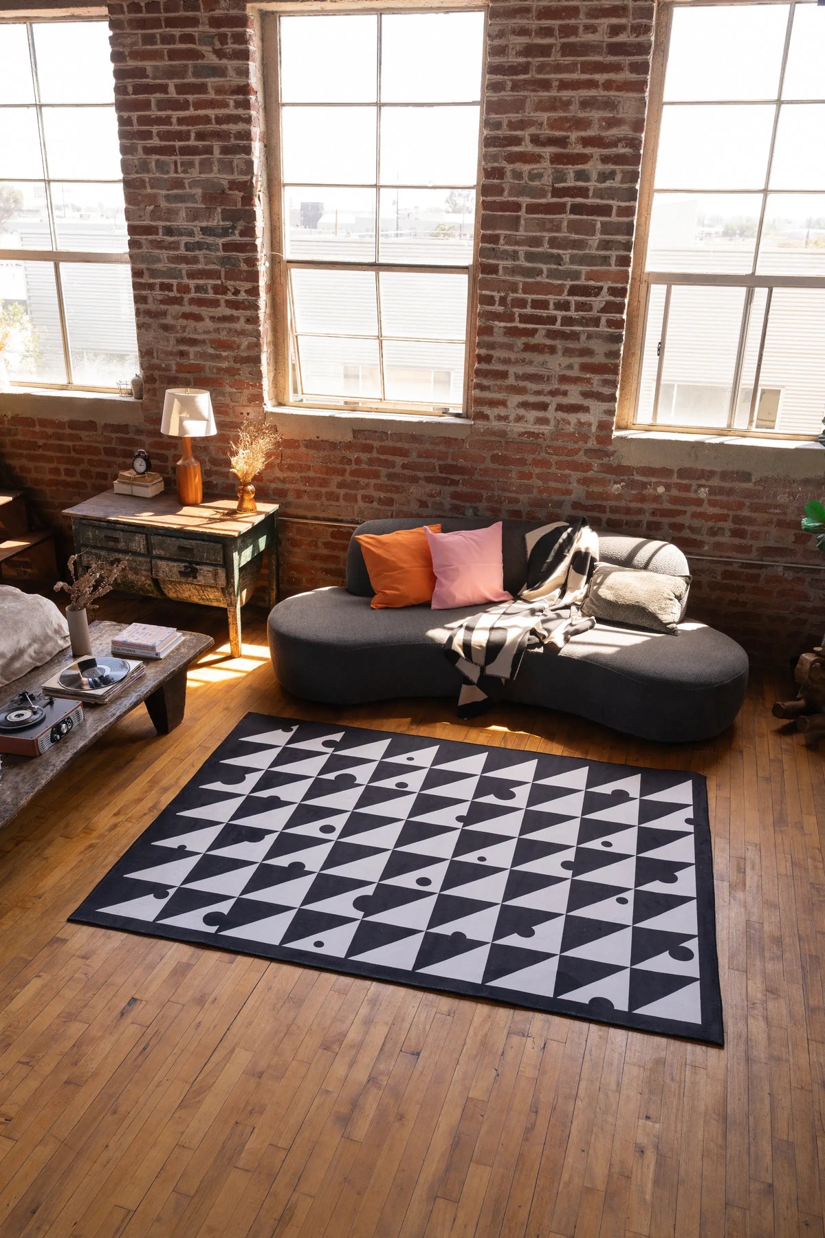 Modern loft interior with a Black & White Triangle Dance Rug centered on wood floor beside a curved grey sofa