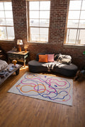 A pastel abstract line rug with intertwined orange, blue, and pink lines sits in a loft living room with large windows