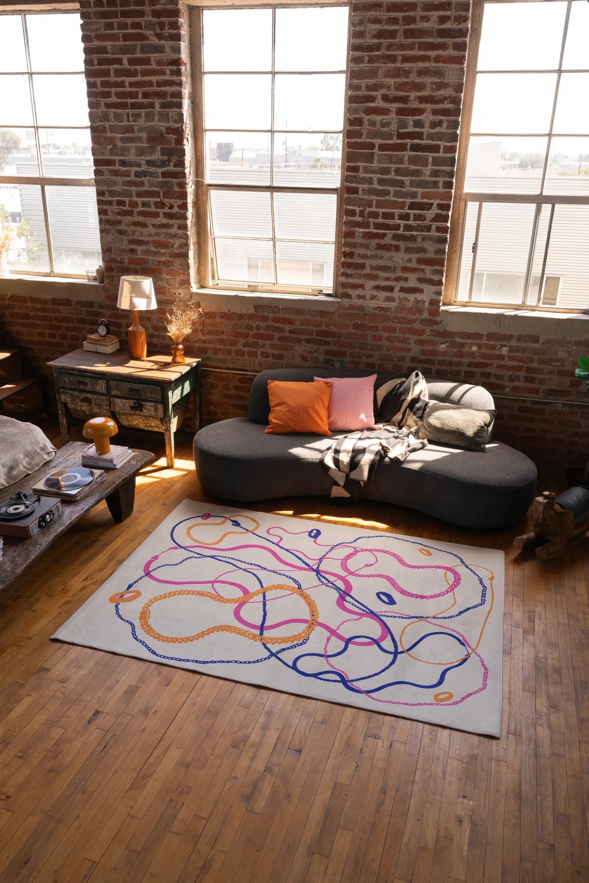 A pastel abstract line rug with intertwined orange, blue, and pink lines sits in a loft living room with large windows