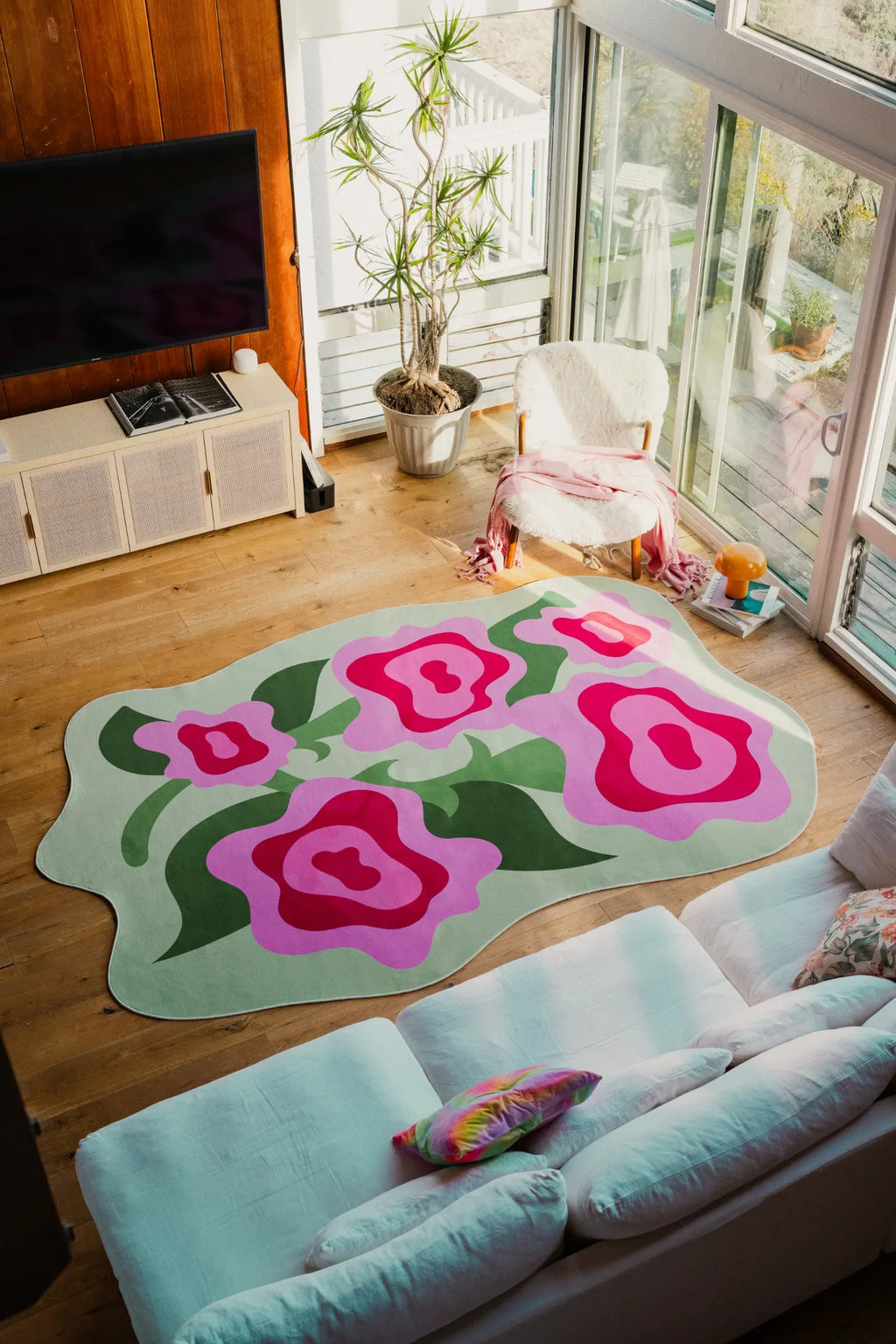 Floral rug with bold rose shapes spread out in a bright corner near sofa and glass doors on wood floor.