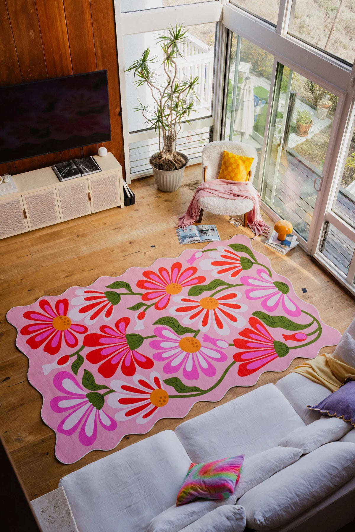 Pink floral wavy rug spread out on light wood floor in a bright corner beside a sofa.