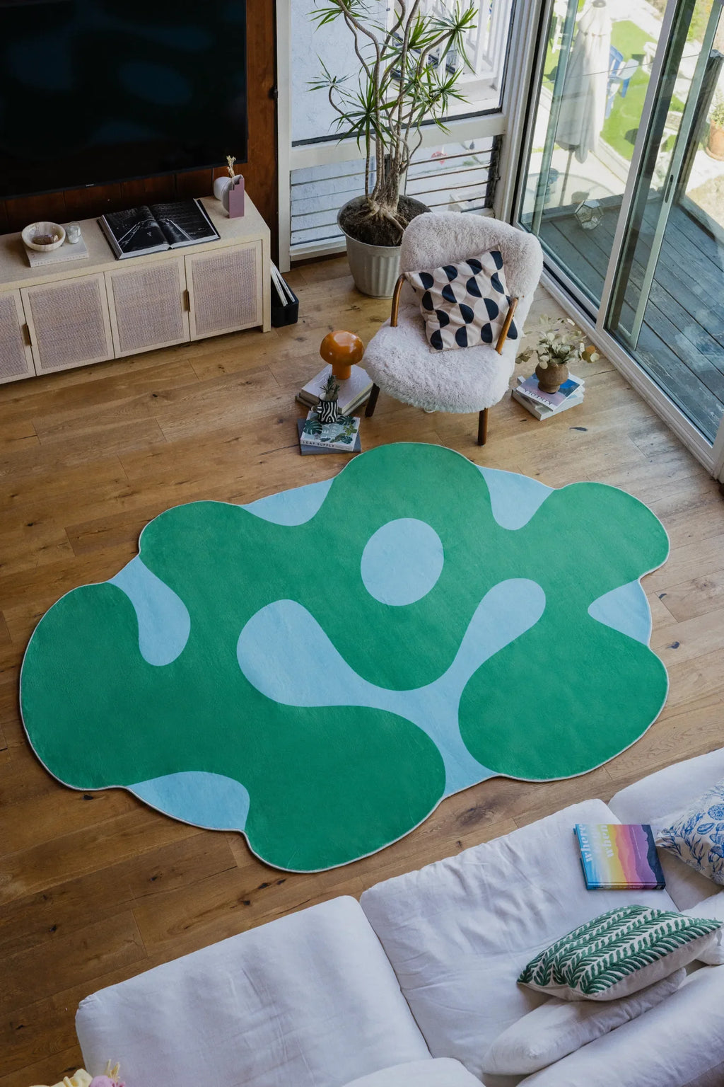 Irregular green moss rug in a sunlit living room with boucle lounge chair, glass doors and indoor plants.