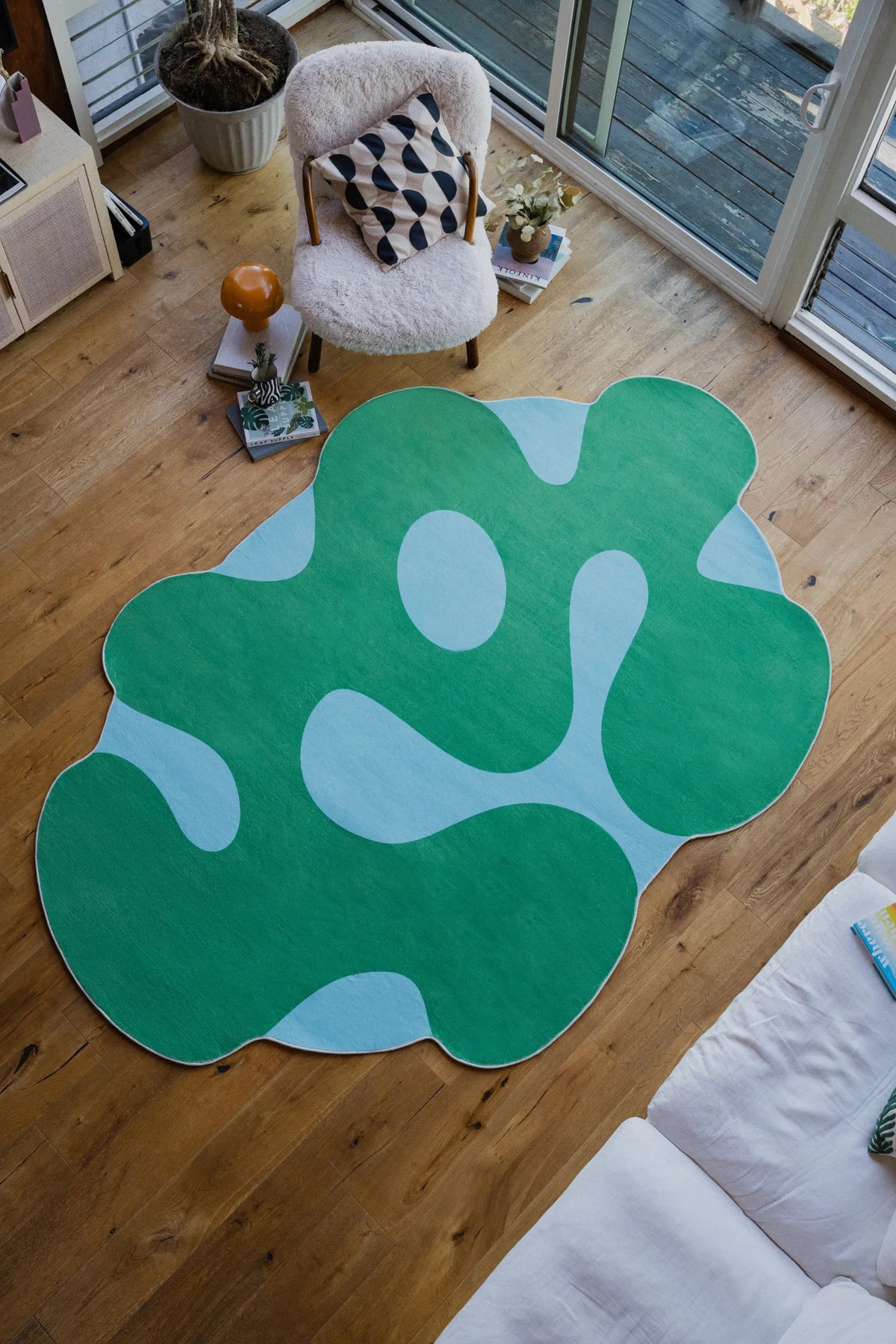 Top view of irregular green moss rug placed in modern living room, highlighting organic shape and soft texture.