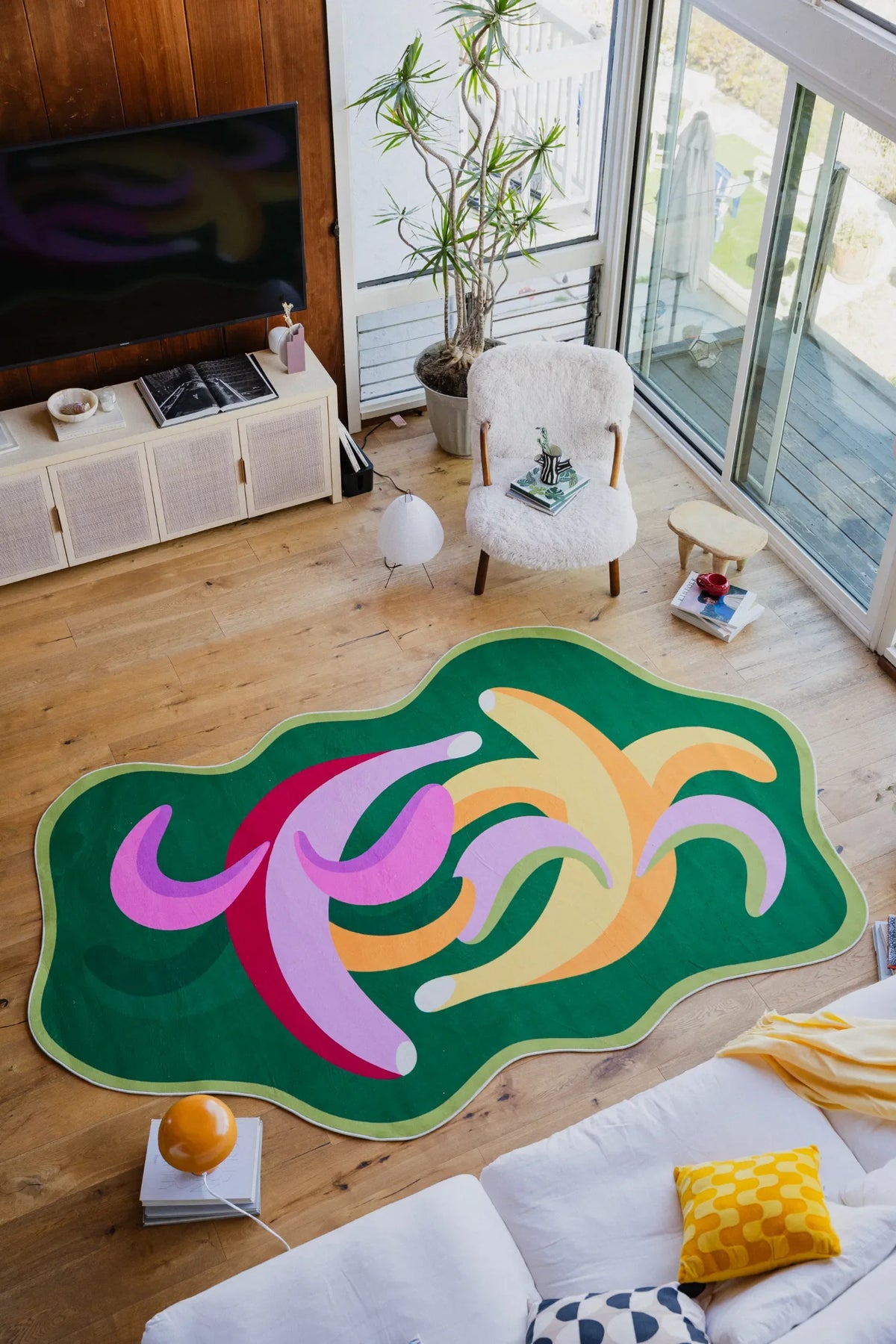 Dancing bananas rug placed in a bright living room next to a boucle chair and potted plant.