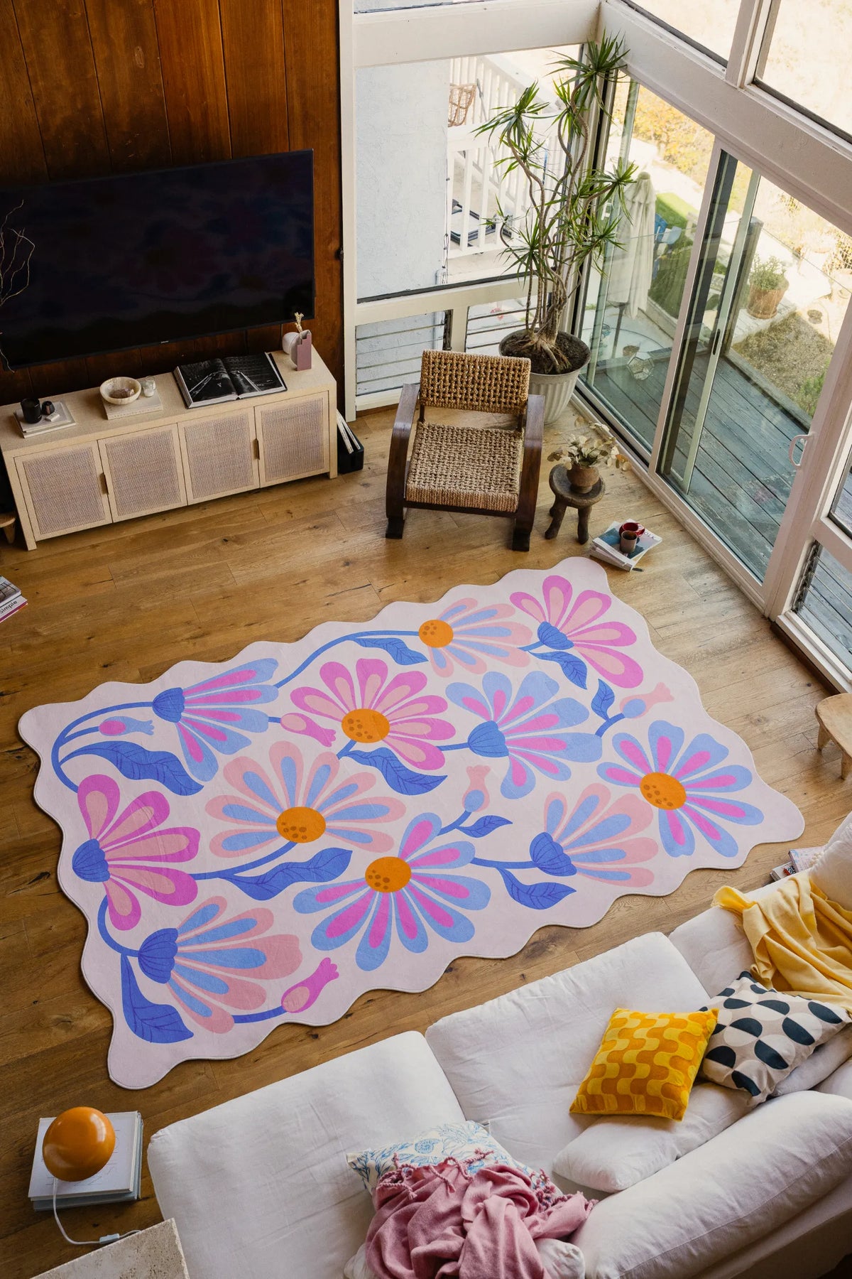Purple floral wavy rug in lilac tones centered on wide plank wood flooring near a rattan chair.