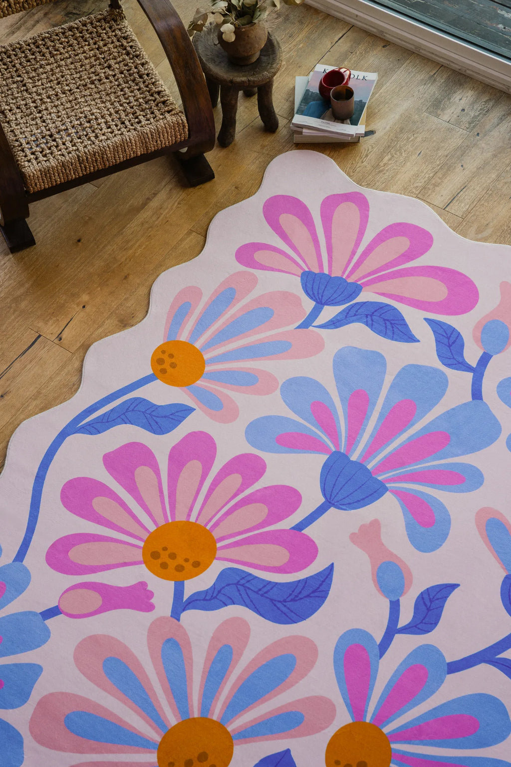 Lilac floral wavy rug beside a woven chair on pale wood flooring near large windows.