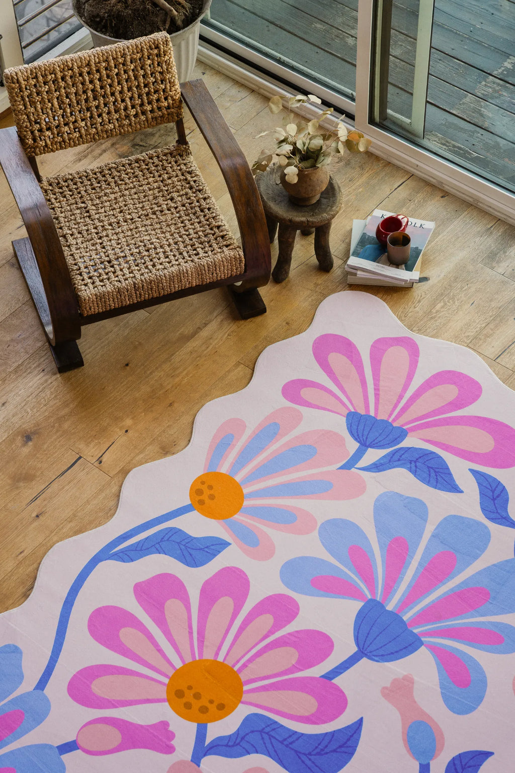 Lilac-toned floral wavy rug partially shown near a woven chair on pale wood floor.