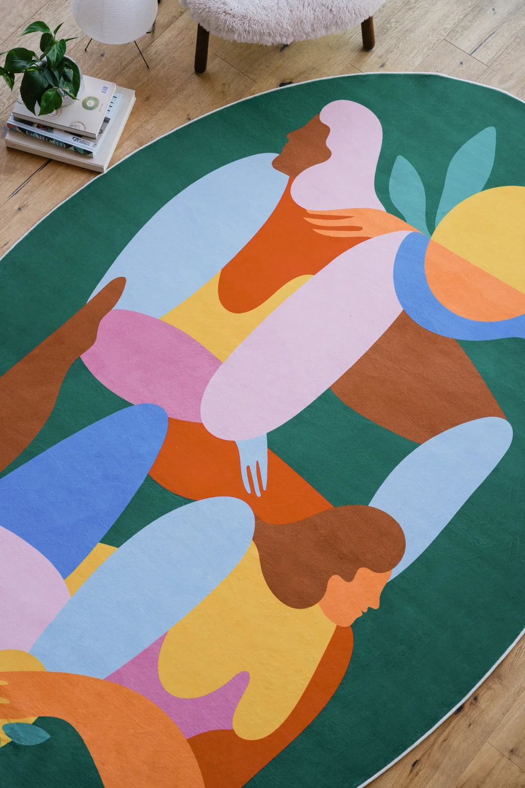 Detail of oval fruitvine green rug showing abstract figures and sun motif near a reading chair.