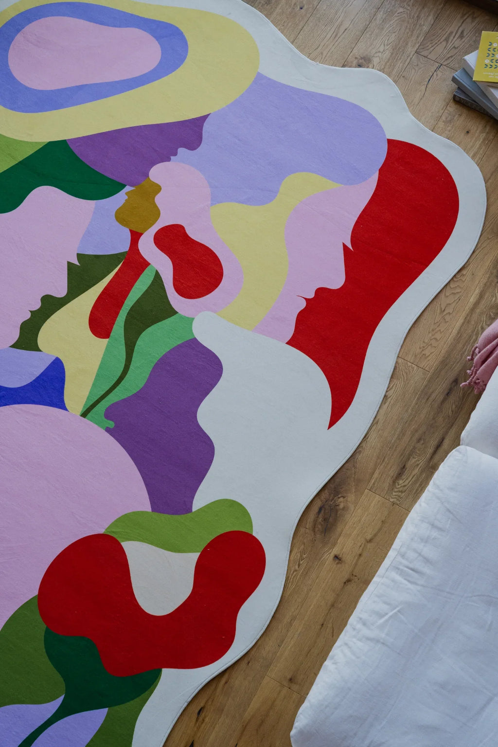 Close-up of the irregular Bloomland Unity rug with face silhouettes in purple, red, and yellow tones on wood floor