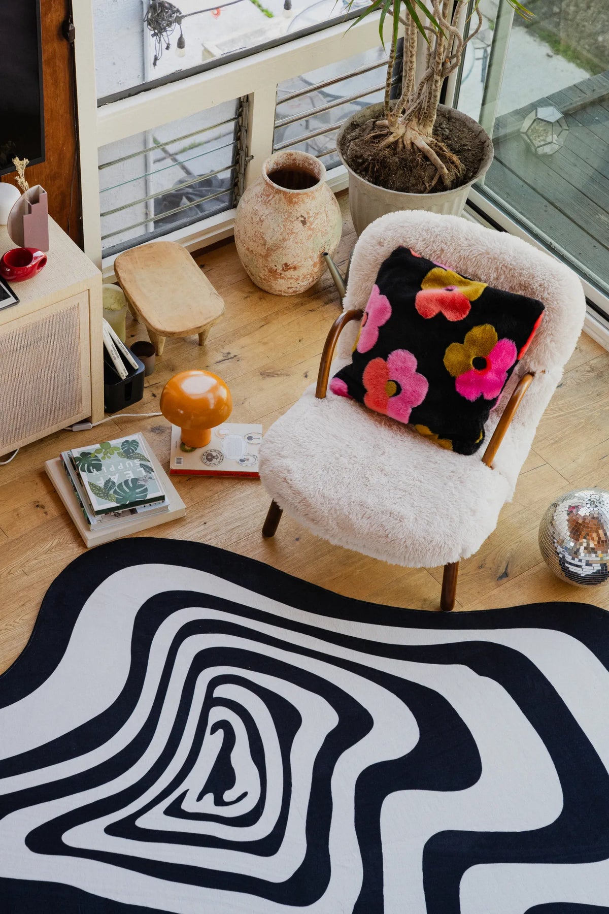 Close-up of the irregular black and white rug near a white fuzzy armchair with a floral pillow.