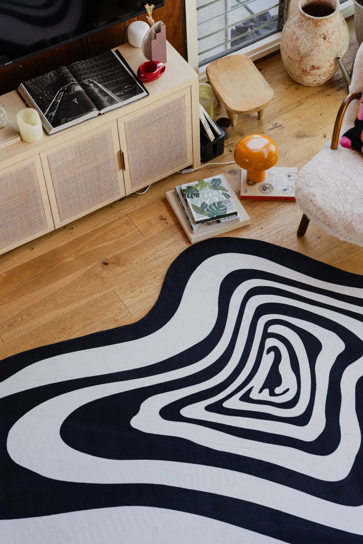 Detail shot of the wavy black and white rug corner, styled with books and decor accessories on wood floor.