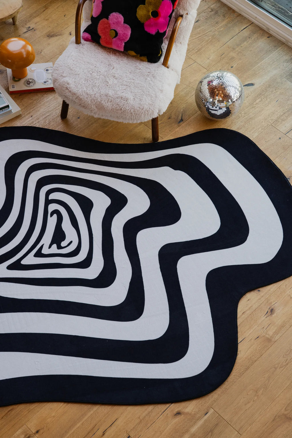 Black and white vertigo rug in a cozy reading nook with boucle chair and floral pillow.
