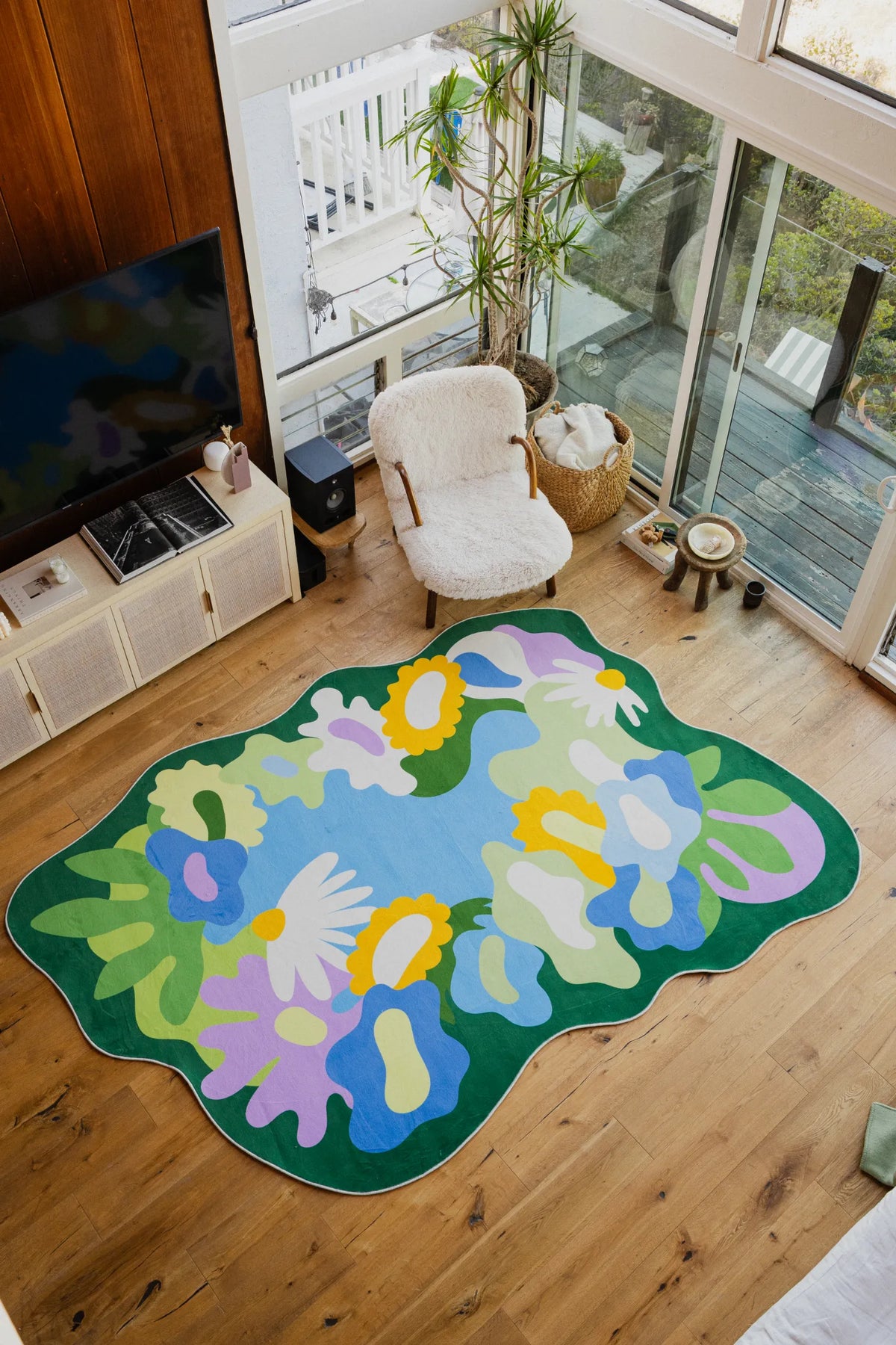 Botanical floral rug with abstract flowers centered in a bright living room, near a chair and glass doors on wood floor.