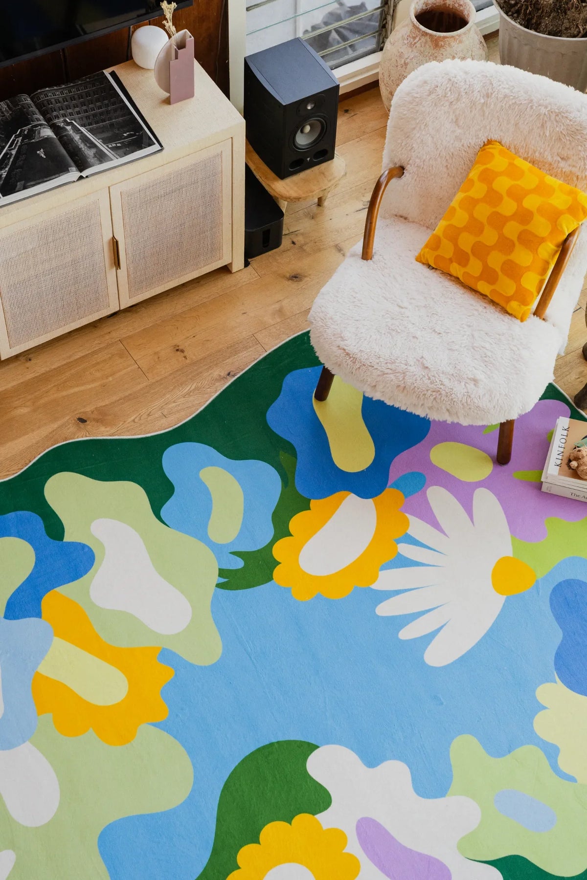 Close-up of floral rug with colorful blooms beside a fuzzy armchair in the living room on light wood floor.