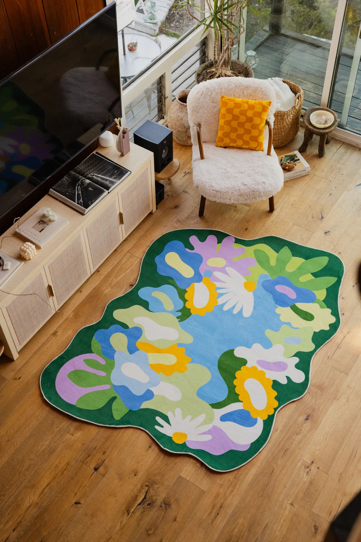 Botanical floral rug laid in a bright living room corner beside a fuzzy chair and TV stand on wood floor.