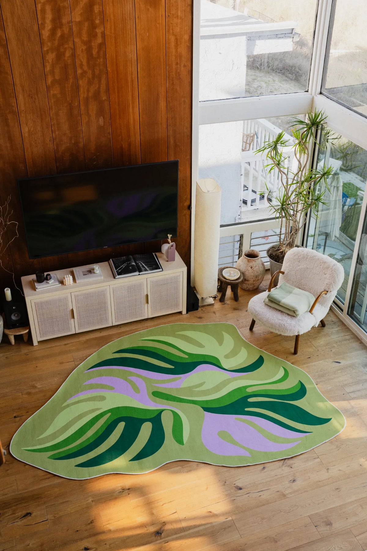 Irregular botanical leaves rug beside a boucle chair and round stools, by the balcony window in soft daylight.