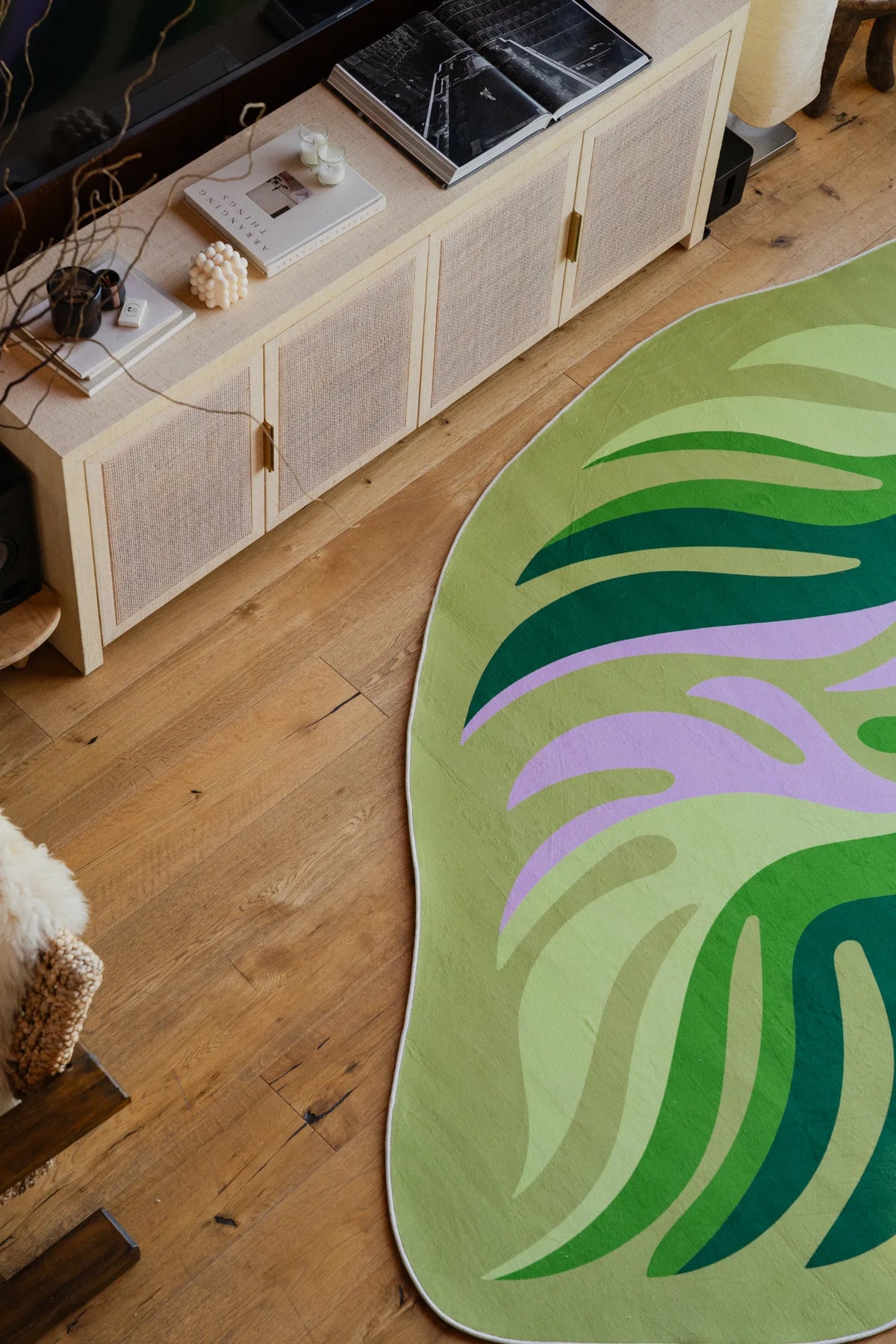 Close-up of botanical leaves rug with books and a red bowl on top, next to a boucle armchair in the living room.