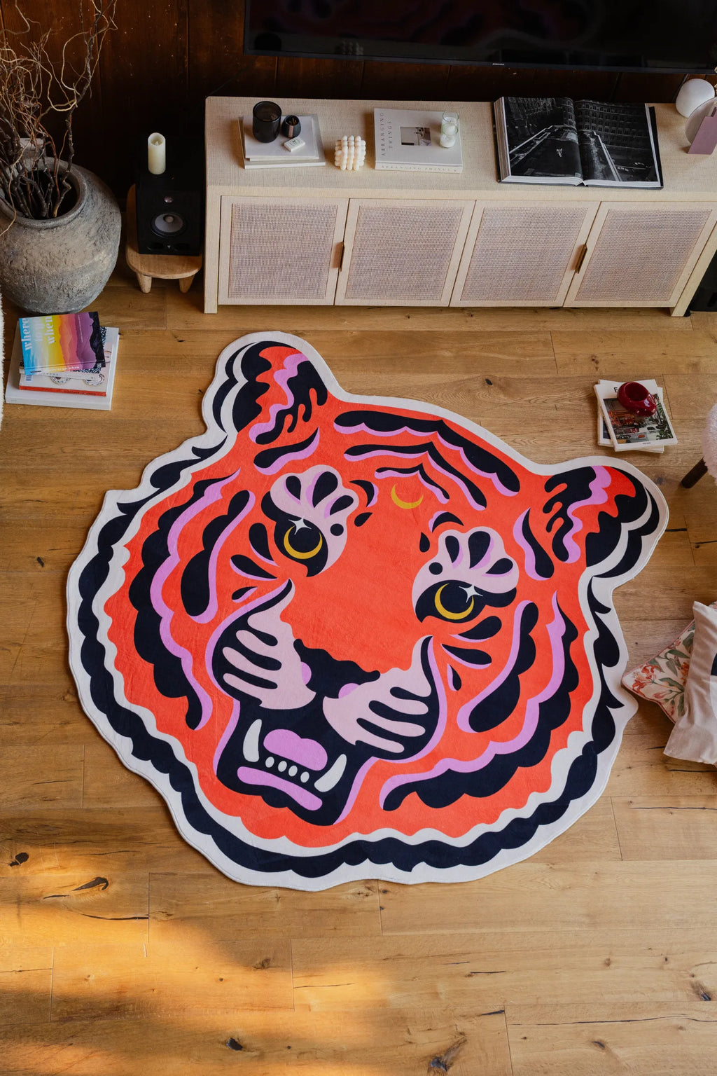 Close-up view of the tiger face rug on hardwood floor, showing its vivid pink, orange, and black tones in a warm nook.
