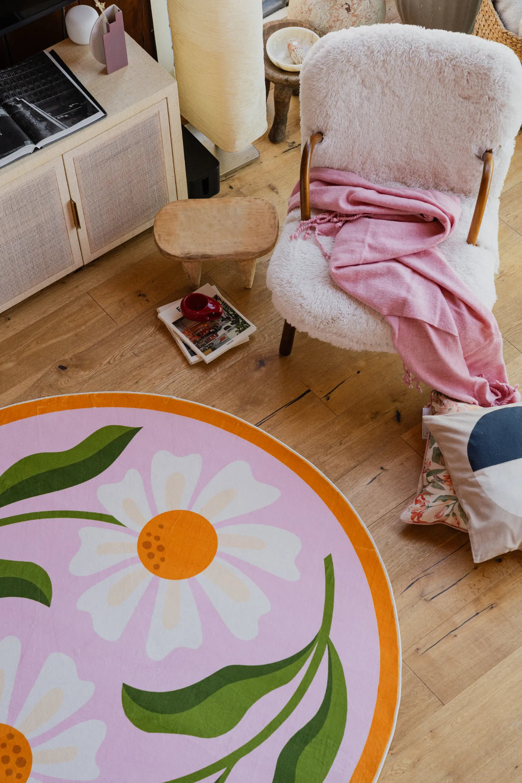 Dual Daisy Pink Round Rug by Jessica Miller partially visible under a stack of books on wooden floor