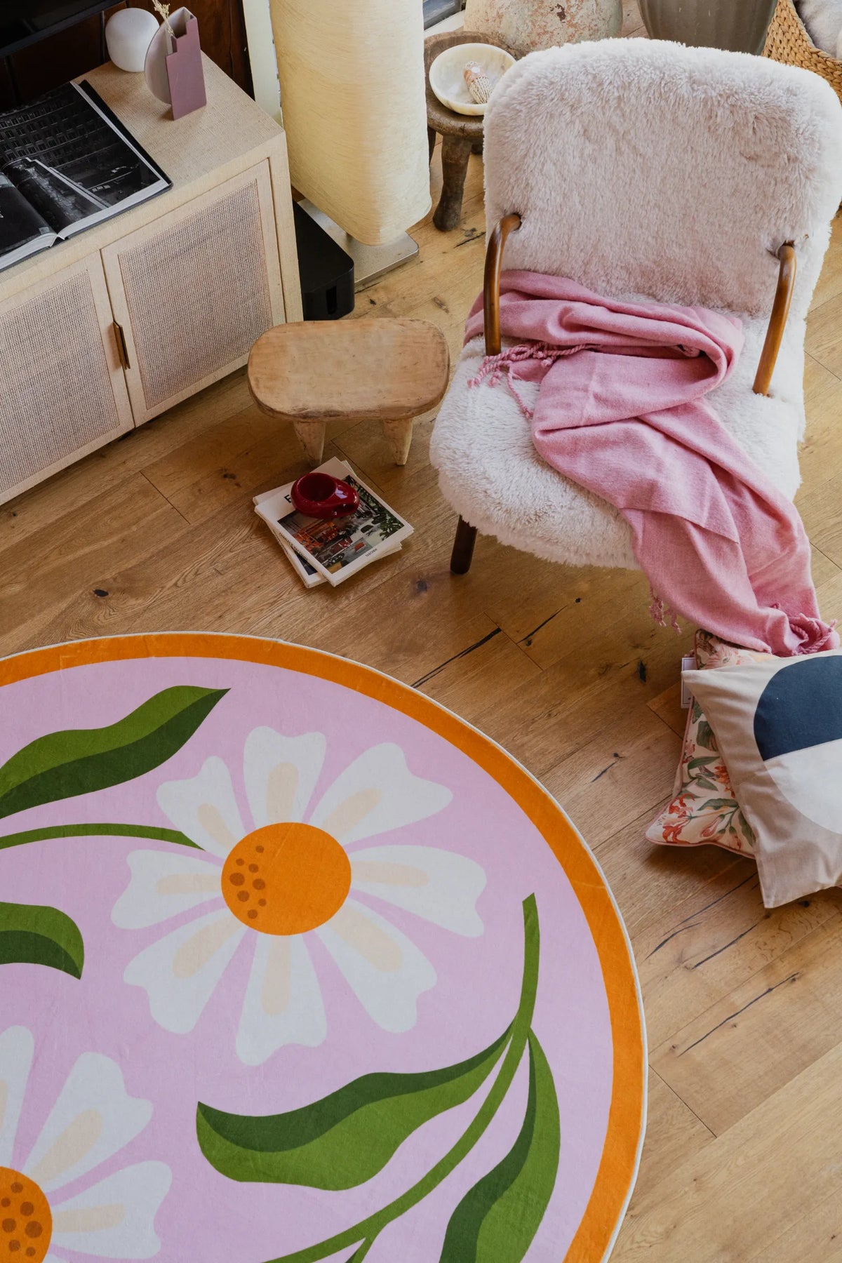 Dual Daisy Pink Round Rug by Jessica Miller partially visible under a stack of books on wooden floor